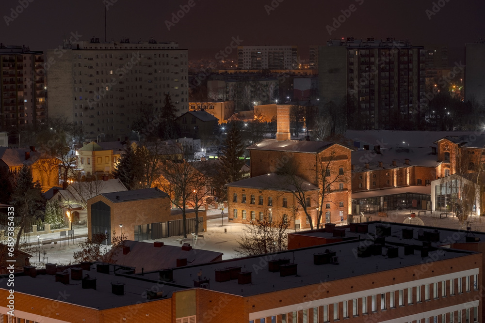 Widok miasta nocą w śniegu . Oświetlone historyczne budynki i nowoczesne bloki mieszkalne . Jesienna noc w Ostrowcu Świętokrzyskim. - obrazy, fototapety, plakaty 
