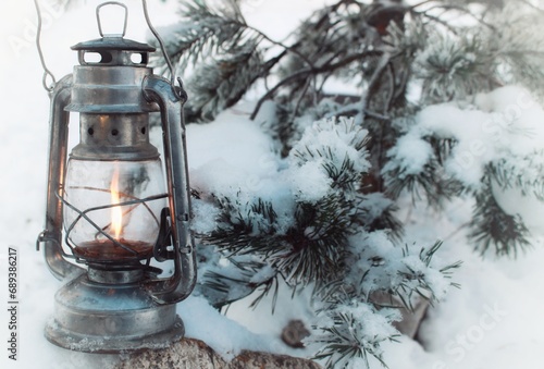 winter kerosene lantern shines in the branches of a pine tree.