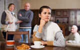 Offended woman sitting by table while her husband and senior parents scolding her