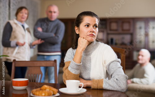 Offended woman sitting by table while her husband and senior parents scolding her