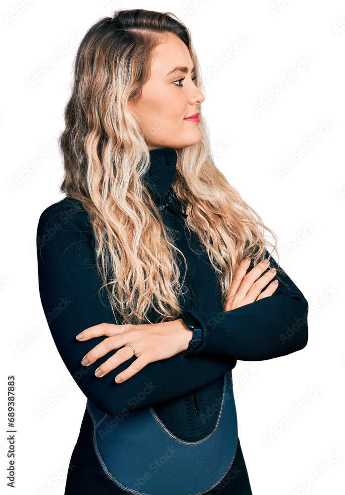 Young blonde woman wearing diver neoprene uniform looking to the side with arms crossed convinced and confident Young blonde woman wearing diver neoprene uniform looking to the side with arms crossed convinced and confident