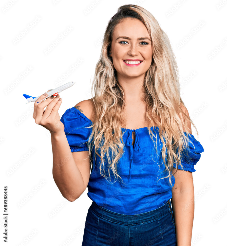Young blonde woman holding airplane toy looking positive and happy standing and smiling with a confident smile showing teeth Young blonde woman holding airplane toy looking positive and happy standing and smiling with a confident smile showing teeth