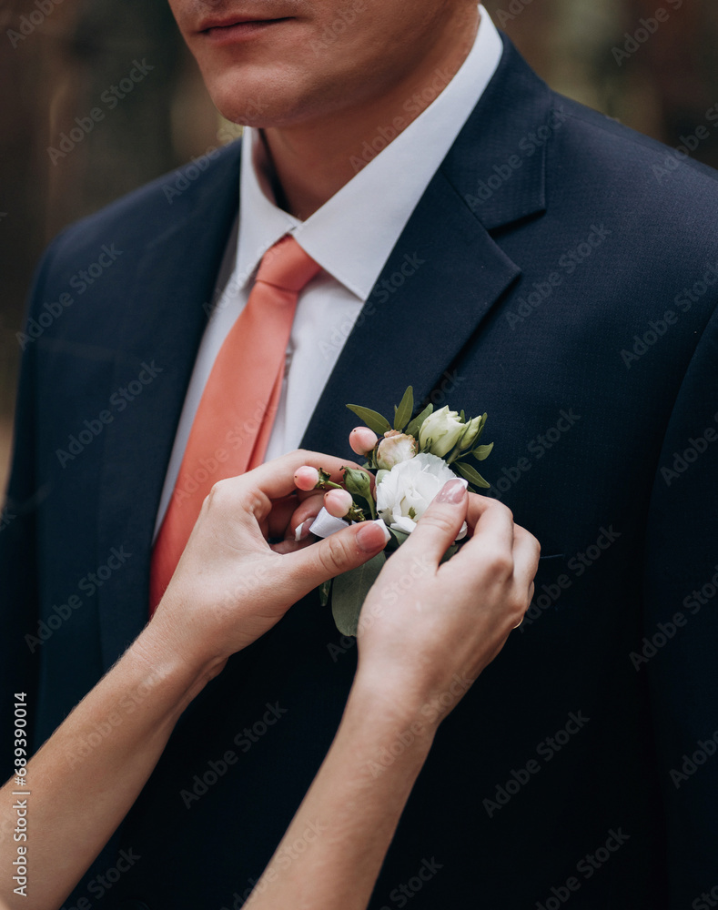 The bride hands touches of the groom's boutonniere on the jacket The bride hands touches of the groom's boutonniere on the jacket