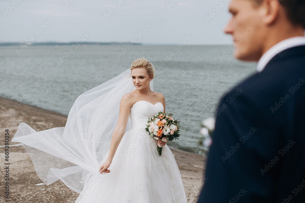 Young and beautiful wedding couple stands near river or lake. Lovely groom and bride on their wedding day.