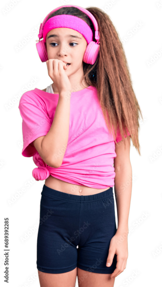 Cute hispanic child girl wearing gym clothes and using headphones looking stressed and nervous with hands on mouth biting nails. anxiety problem. Cute hispanic child girl wearing gym clothes and using headphones looking stressed and nervous with hands on mouth biting nails. anxiety problem.