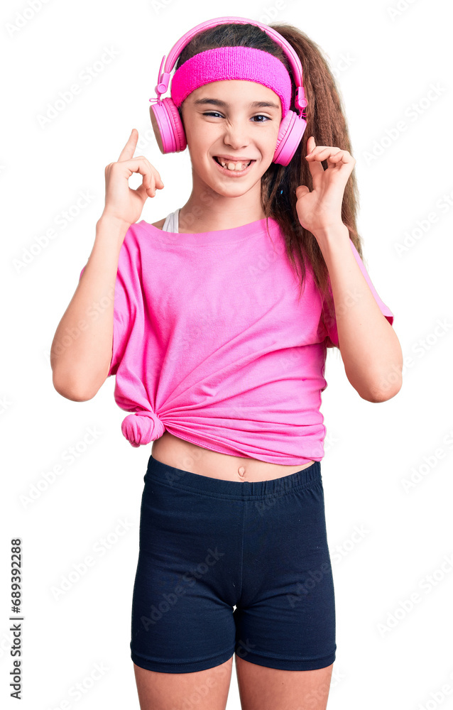 Cute hispanic child girl wearing gym clothes and using headphones covering ears with fingers with annoyed expression for the noise of loud music. deaf concept. Cute hispanic child girl wearing gym clothes and using headphones covering ears with fingers with annoyed expression for the noise of loud music. deaf concept.