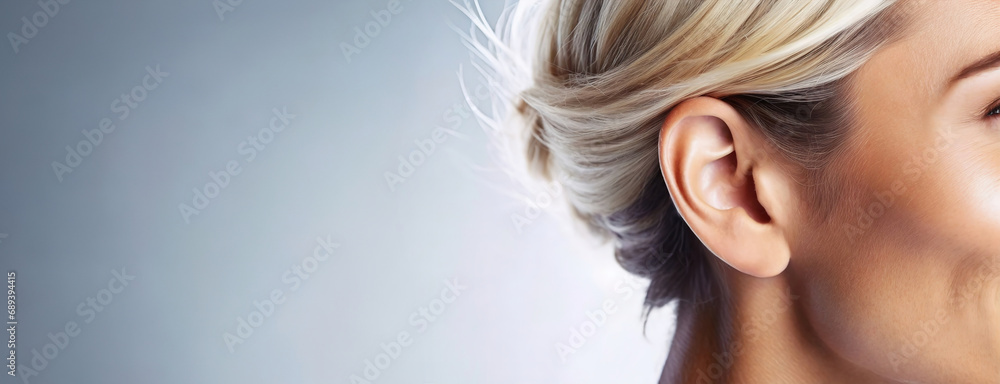 A woman's ear visible on a clear background with copy space. Side view of a woman's head showing her ear and the back of her sleek blonde hair, spacious clear background.