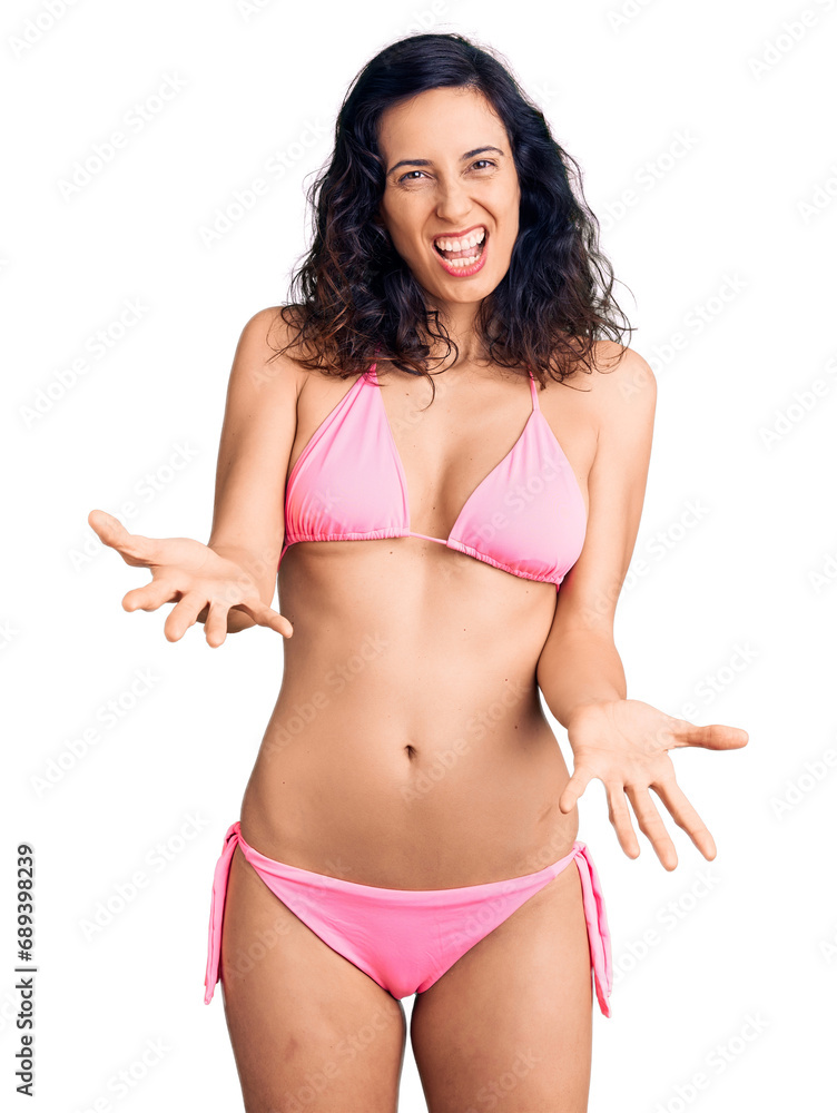 Young beautiful hispanic woman wearing bikini smiling cheerful with open arms as friendly welcome, positive and confident greetings Young beautiful hispanic woman wearing bikini smiling cheerful with open arms as friendly welcome, positive and confident greetings