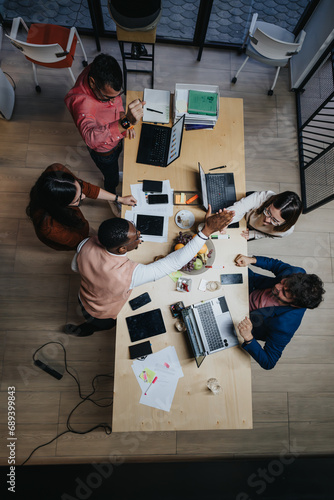 Above view photo of multicultural team collaborating in office, discussing project details, analyzing stats for business growth. photo