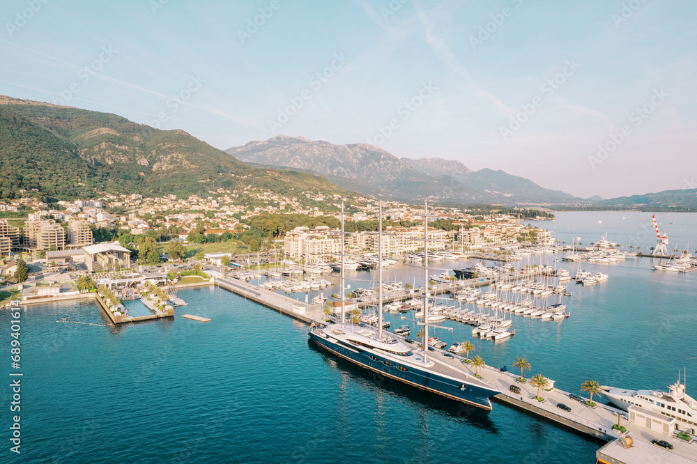 Expensive sailing yacht is moored at the pier overlooking the modern hotels on the shore. Porto, Montenegro. Drone