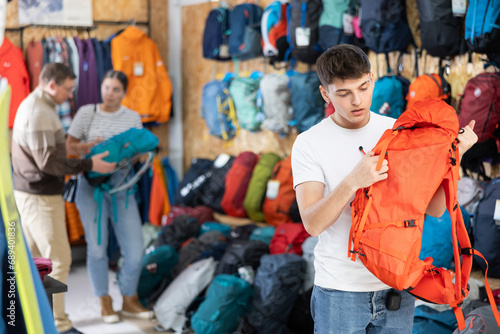 Guy chooses and buys tourist backpack for summer hike in a sports equipment store