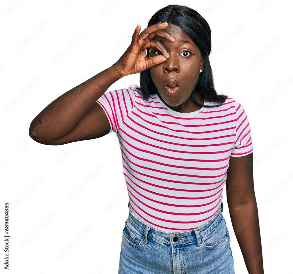 African young woman wearing casual striped t shirt doing ok gesture shocked with surprised face, eye looking through fingers. unbelieving expression. African young woman wearing casual striped t shirt doing ok gesture shocked with surprised face, eye looking through fingers. unbelieving expression.