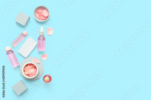 Plaster podiums with bottles of essential oil and rose petals on blue background
