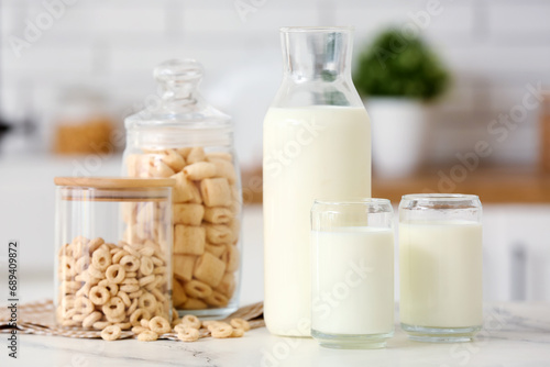Glasses and bottle of fresh milk with cereal rings on white table