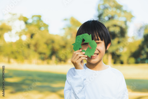 Cheerful young asian boy holding recycle symbol on daylight natural green park promoting waste recycle  reduce  and reuse encouragement for eco sustainable awareness for future generation. Gyre