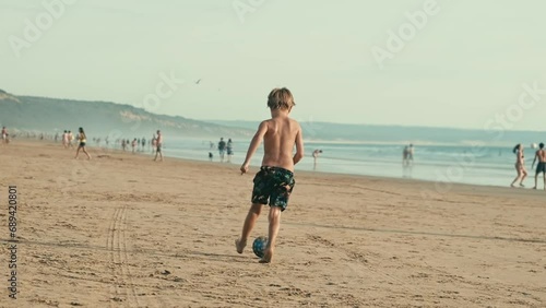 Boy having fun playing running with ball on the beach of Atlantic Ocean. Fonta da Telha beach, Costa da Caparica, Portugal photo