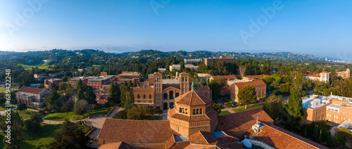 Aerial view of UCLA campus in Westwood, Los Angeles, featuring red-brick, Gothic, and modern buildings amidst green lawns and trees on a sunny day.