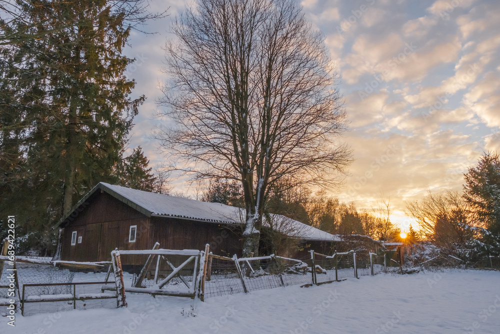 Old farm in the countryside at winter covered with snow at sunset.