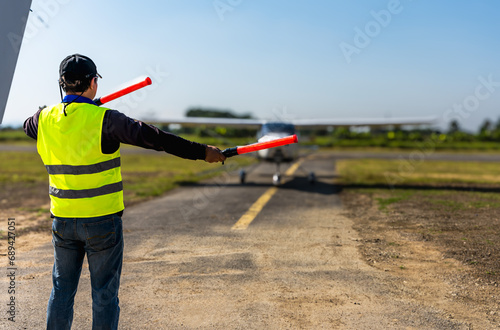 Back view aircraft controller man with gesture sticks control small plane in airfield