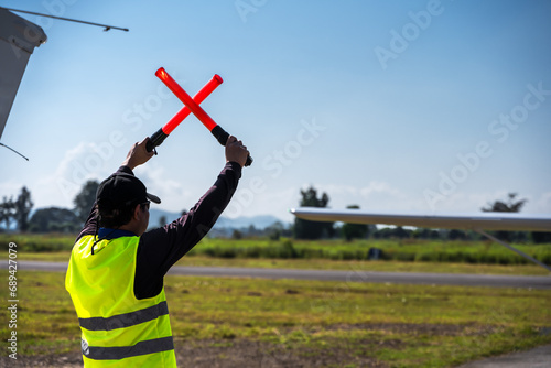 Slika na platnu Back view airport ground crew with gesturing sticks controlling small plane in a