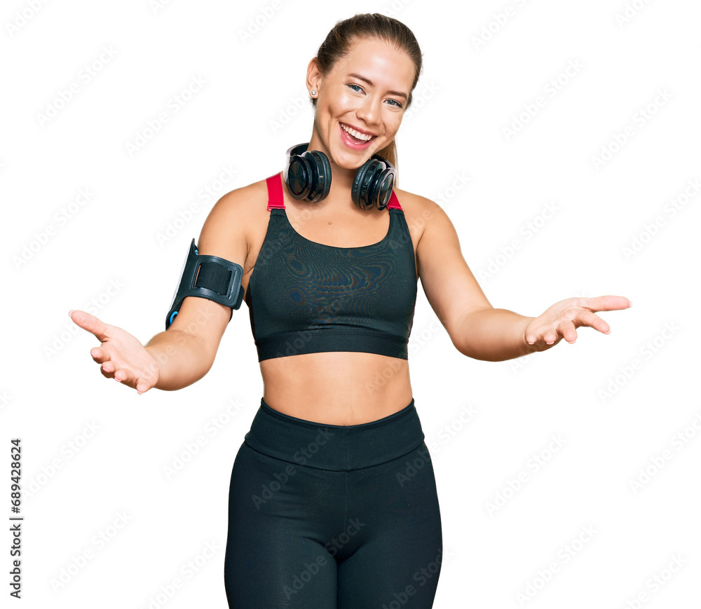 Beautiful blonde woman wearing gym clothes and using headphones smiling cheerful offering hands giving assistance and acceptance. Beautiful blonde woman wearing gym clothes and using headphones smiling cheerful offering hands giving assistance and acceptance.