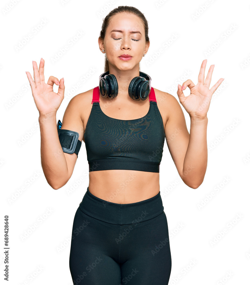 Beautiful blonde woman wearing gym clothes and using headphones relaxed and smiling with eyes closed doing meditation gesture with fingers. yoga concept. Beautiful blonde woman wearing gym clothes and using headphones relaxed and smiling with eyes closed doing meditation gesture with fingers. yoga concept.