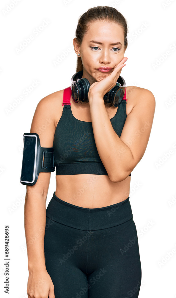 Beautiful blonde woman wearing gym clothes and using headphones thinking looking tired and bored with depression problems with crossed arms. Beautiful blonde woman wearing gym clothes and using headphones thinking looking tired and bored with depression problems with crossed arms.