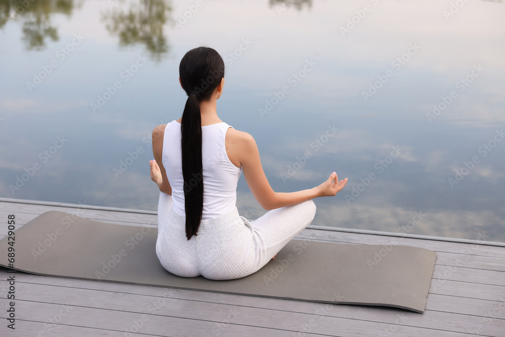 Woman practicing Padmasana on yoga mat outdoors, back view. Lotus pose