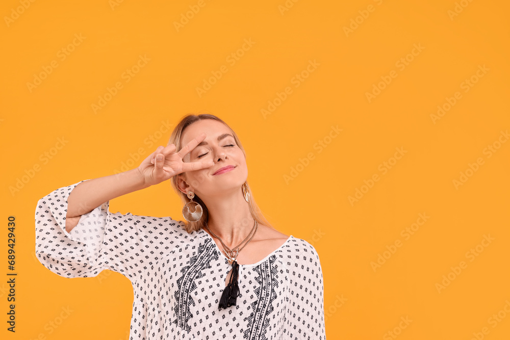 Portrait of hippie woman showing peace sign on yellow background. Space for text Portrait of hippie woman showing peace sign on yellow background. Space for text