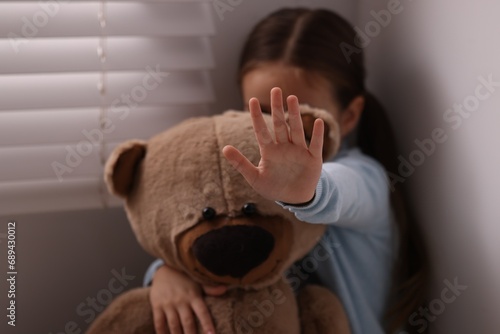 Child abuse. Little girl with teddy bear doing stop gesture indoors, selective focus photo