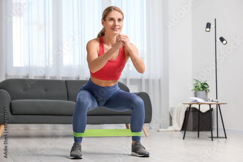 Fit woman doing squats with fitness elastic band at home