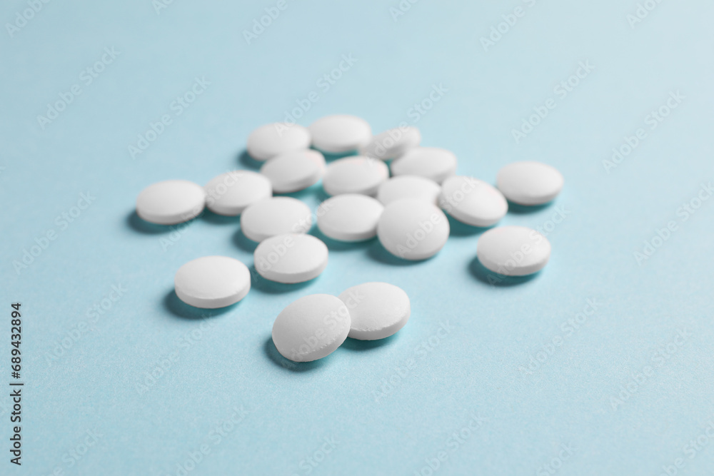 Many white pills on light blue background, closeup Many white pills on light blue background, closeup