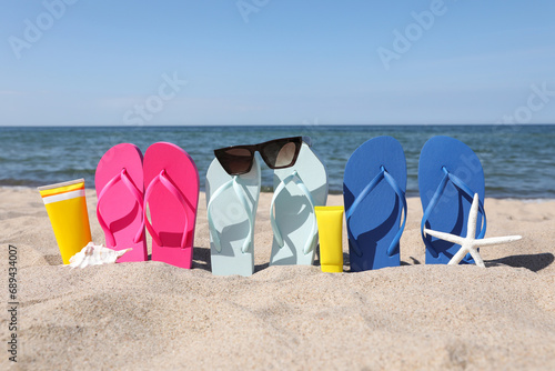 Stylish colorful flip flops with sunglasses and sunscreens on beach sand