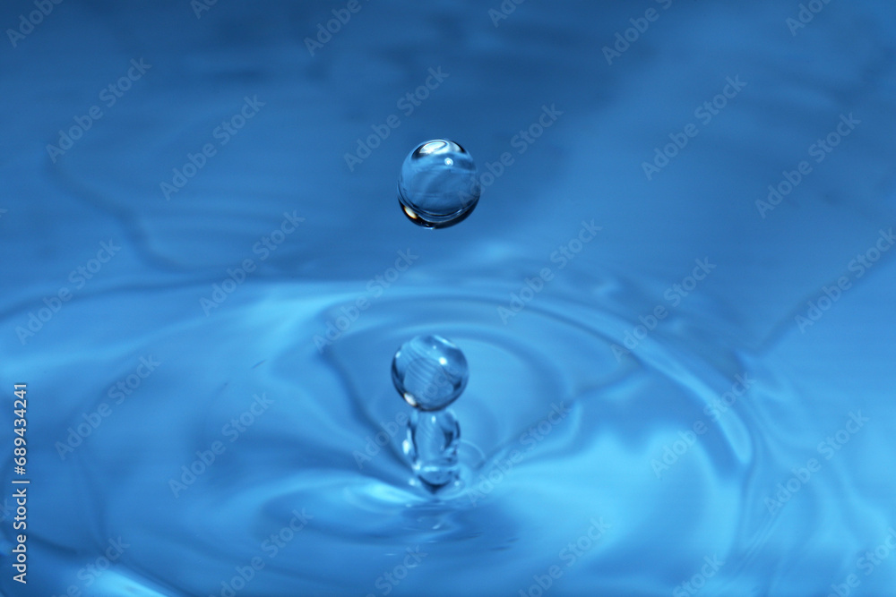 Drop falling into water on blue background, macro view