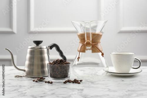 Glass chemex coffeemaker, kettle, beans in bowl and cup on white marble table photo
