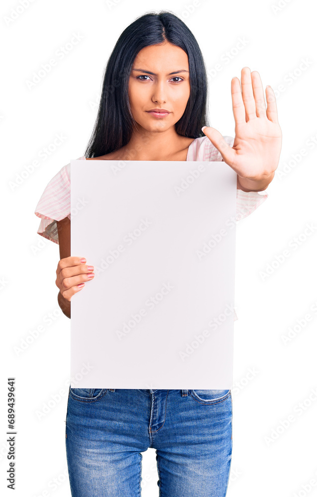Young beautiful latin girl holding blank empty banner with open hand doing stop sign with serious and confident expression, defense gesture Young beautiful latin girl holding blank empty banner with open hand doing stop sign with serious and confident expression, defense gesture