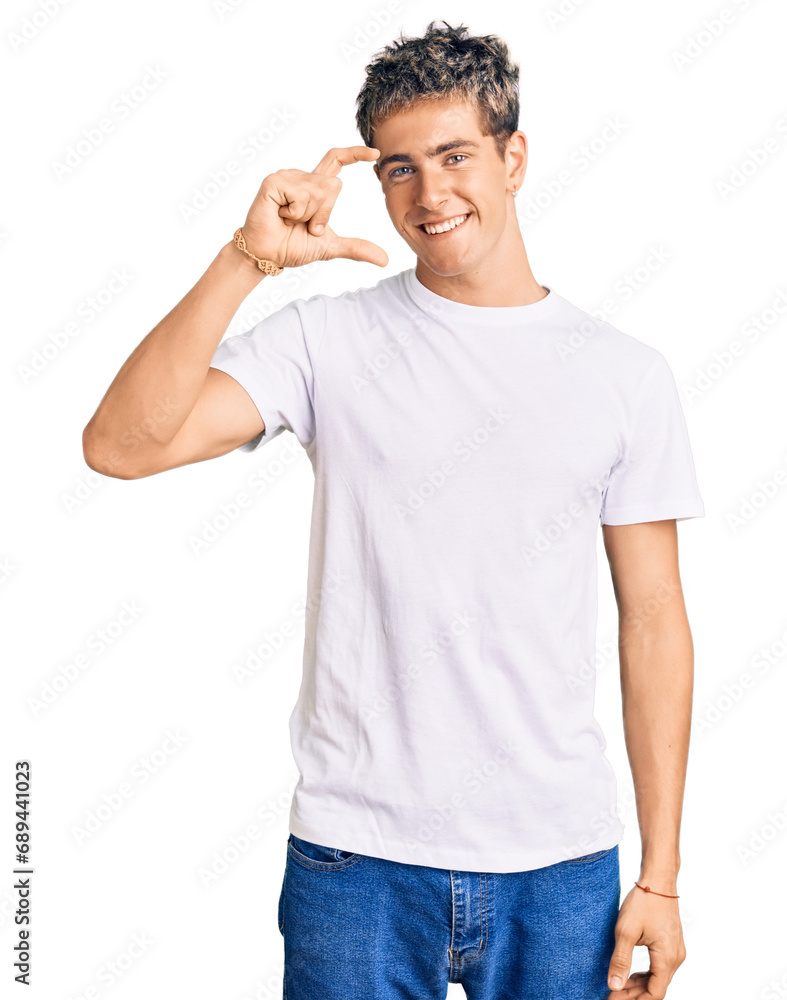 Young handsome man wearing casual white tshirt smiling and confident gesturing with hand doing small size sign with fingers looking and the camera. measure concept. Young handsome man wearing casual white tshirt smiling and confident gesturing with hand doing small size sign with fingers looking and the camera. measure concept.