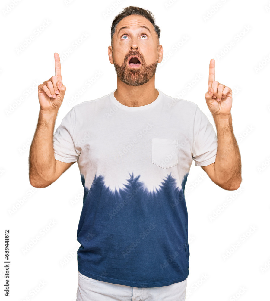 Handsome middle age man wearing casual tie dye tshirt amazed and surprised looking up and pointing with fingers and raised arms. Handsome middle age man wearing casual tie dye tshirt amazed and surprised looking up and pointing with fingers and raised arms.