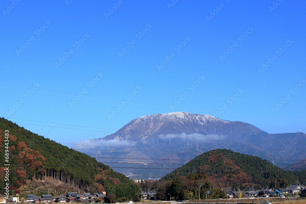 紅葉した山の奥に見える雪が積もった伊吹山と山腹に浮かぶ雲　青空の背景