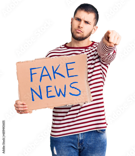 Young handsome man holding fake news message banner pointing with finger to the camera and to you, confident gesture looking serious