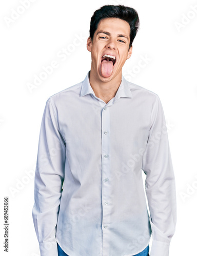 Young hispanic business man wearing business clothes sticking tongue out happy with funny expression. emotion concept.
