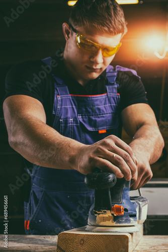 Portrait of a  young man  carpenter using electric sanding machine to polish a wood barin workshop photo