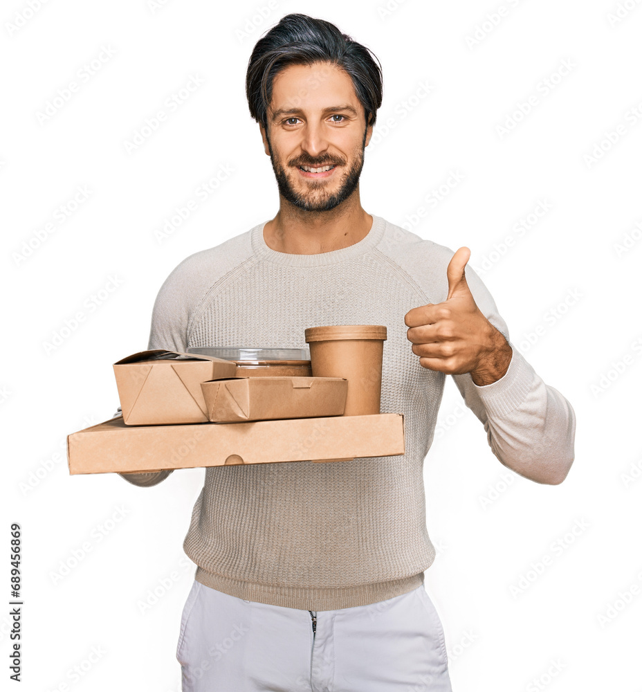 Young hispanic man holding take away food smiling happy and positive, thumb up doing excellent and approval sign Young hispanic man holding take away food smiling happy and positive, thumb up doing excellent and approval sign