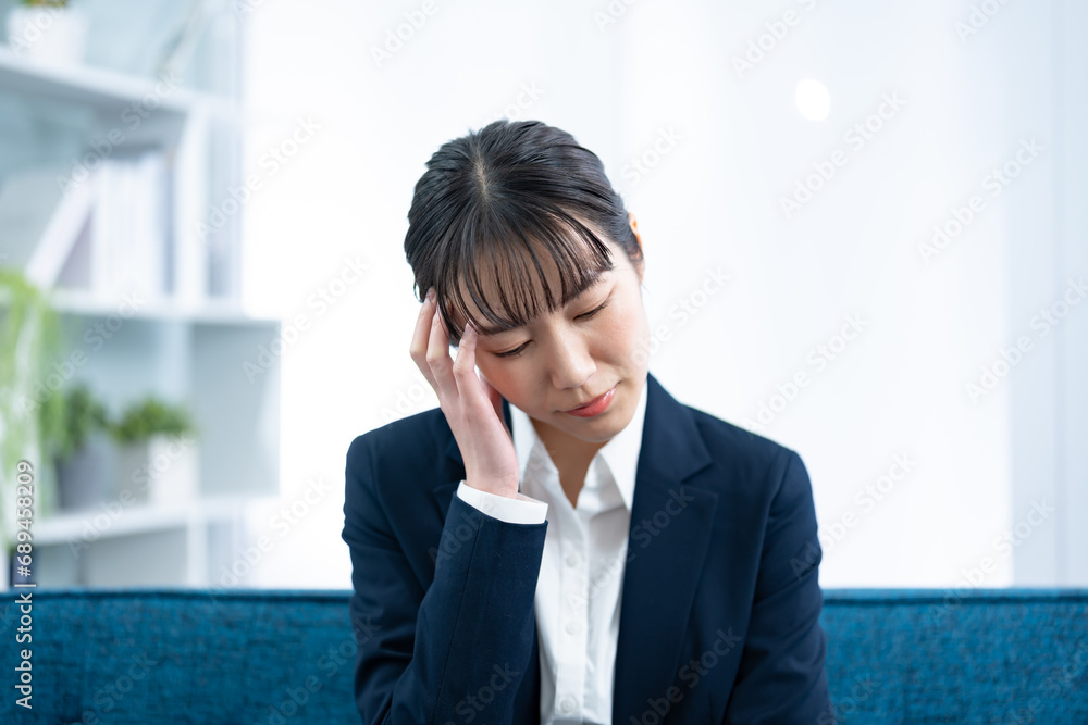 ソファで頭をおさえるスーツを着た日本人女性