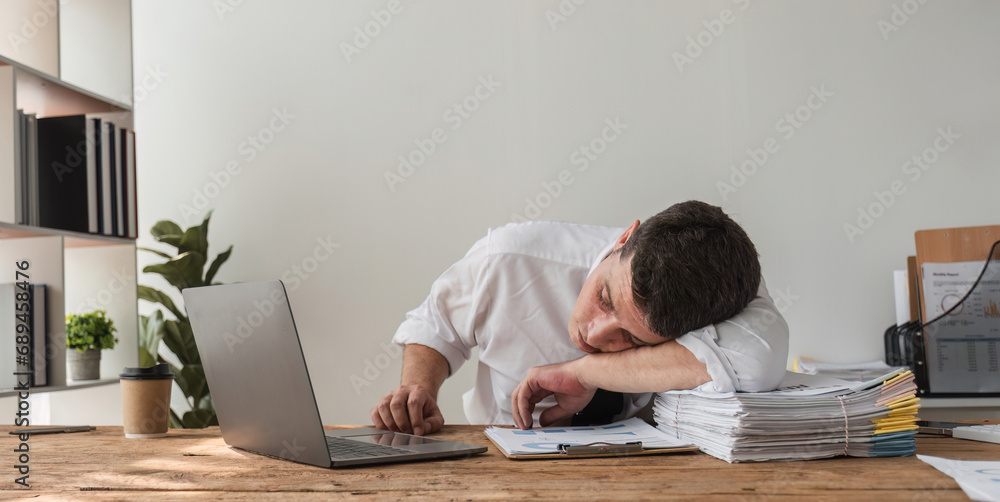 Obraz premium Unhappy young office worker feeling bored at work looking at laptop with a hopeless expression while sitting in the office. Male office worker feeling tired from monotonous work.