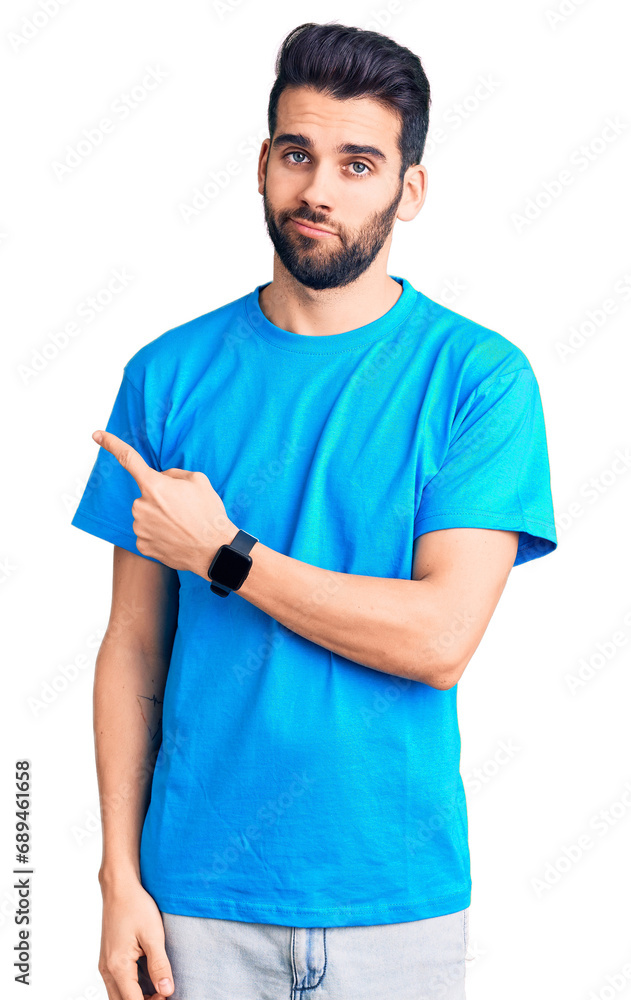 Young handsome man with beard wearing casual t-shirt pointing with hand finger to the side showing advertisement, serious and calm face Young handsome man with beard wearing casual t-shirt pointing with hand finger to the side showing advertisement, serious and calm face