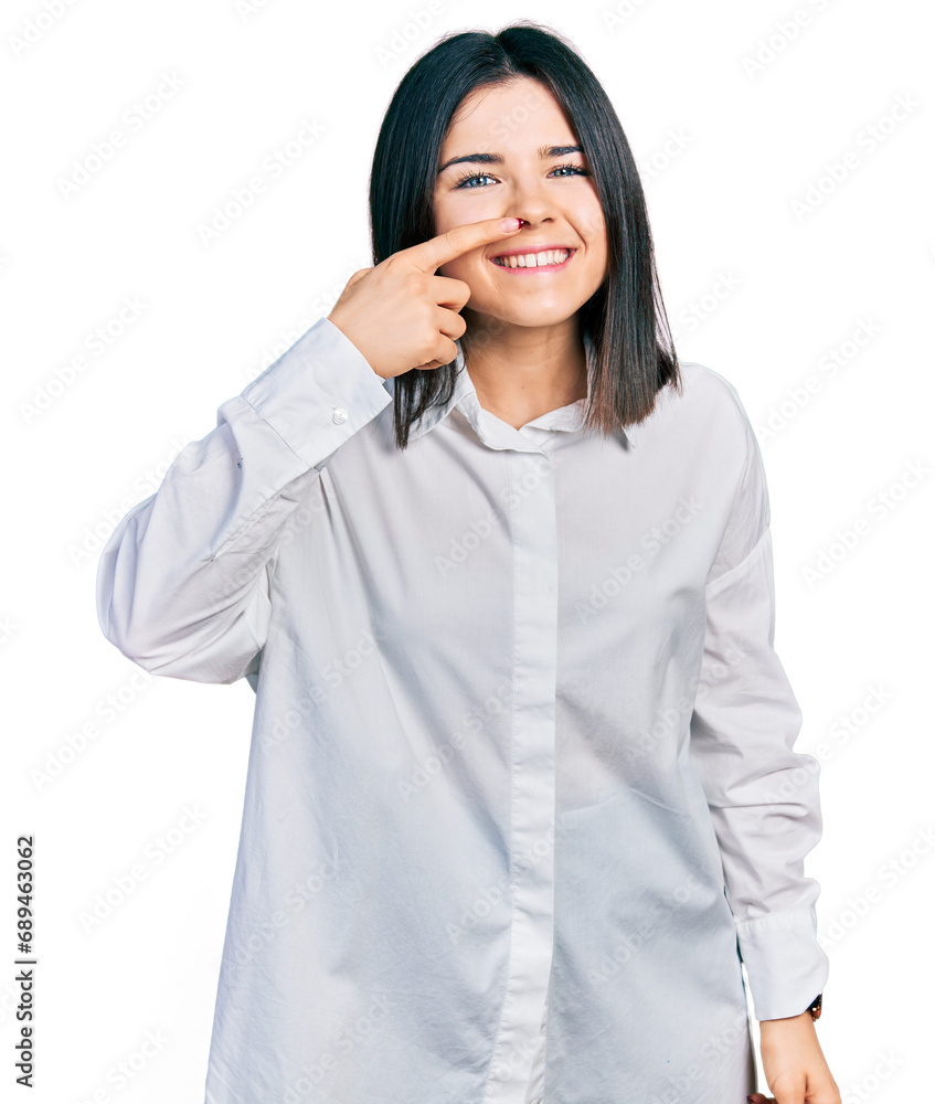 Young brunette woman with blue eyes wearing oversize white shirt pointing with hand finger to face and nose, smiling cheerful. beauty concept Young brunette woman with blue eyes wearing oversize white shirt pointing with hand finger to face and nose, smiling cheerful. beauty concept