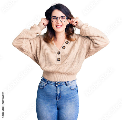 Beautiful young brunette woman wearing casual clothes and glasses smiling pulling ears with fingers, funny gesture. audition problem