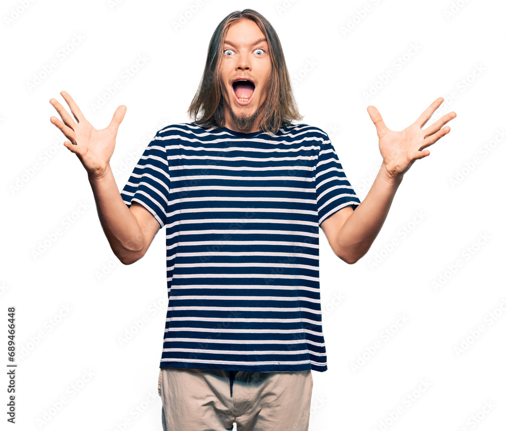 Handsome caucasian man with long hair wearing casual striped t-shirt celebrating crazy and amazed for success with arms raised and open eyes screaming excited. winner concept Handsome caucasian man with long hair wearing casual striped t-shirt celebrating crazy and amazed for success with arms raised and open eyes screaming excited. winner concept