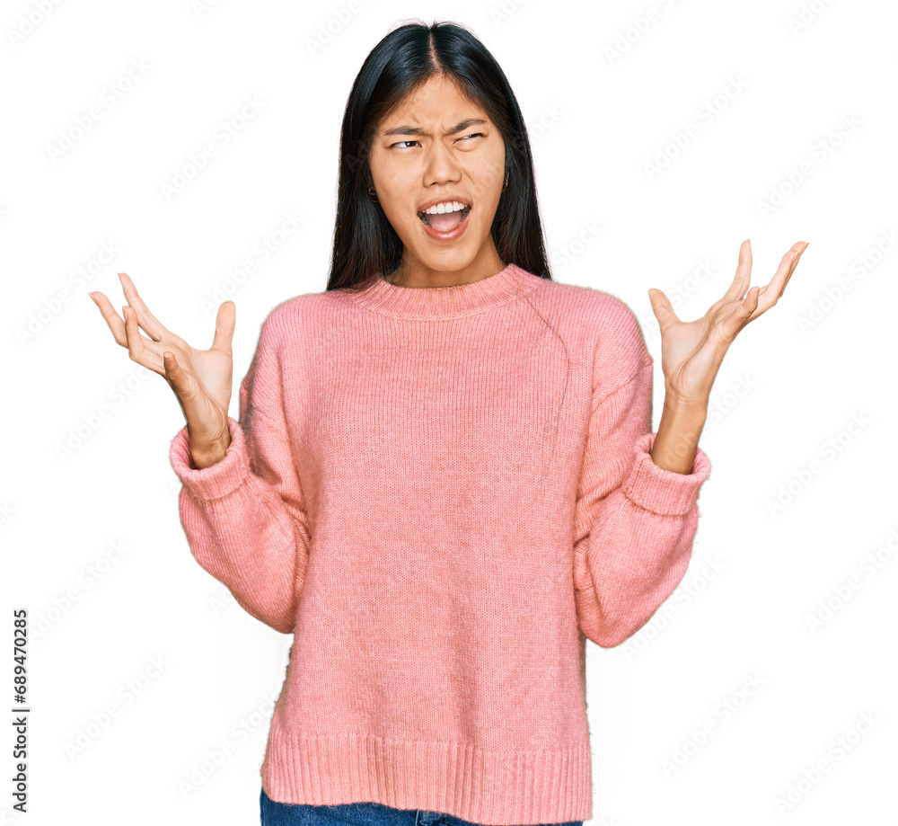 Beautiful young asian woman wearing casual winter sweater crazy and mad shouting and yelling with aggressive expression and arms raised. frustration concept. Beautiful young asian woman wearing casual winter sweater crazy and mad shouting and yelling with aggressive expression and arms raised. frustration concept.